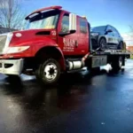 A red Bill's Towing flatbed truck loaded with a black SUV parked on a wet surface in Eugene, Oregon.