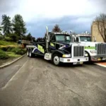A black Bill's Towing heavy-duty wrecker parked next to a white semi tow truck on a paved road.