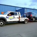 A Bill's Towing truck towing a black SUV using safety dollies next to a blue commercial building in Sutherlin, Oregon.